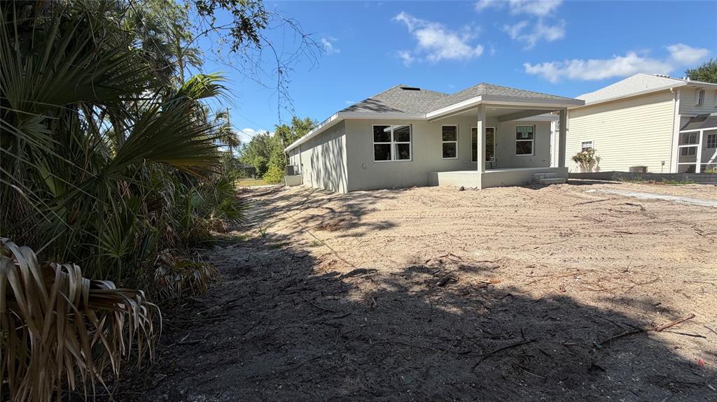 The exterior rear view of a single-story house features a covered patio and sandy yard — 17492 QUINCY AVENUE, PORT CHARLOTTE, FL