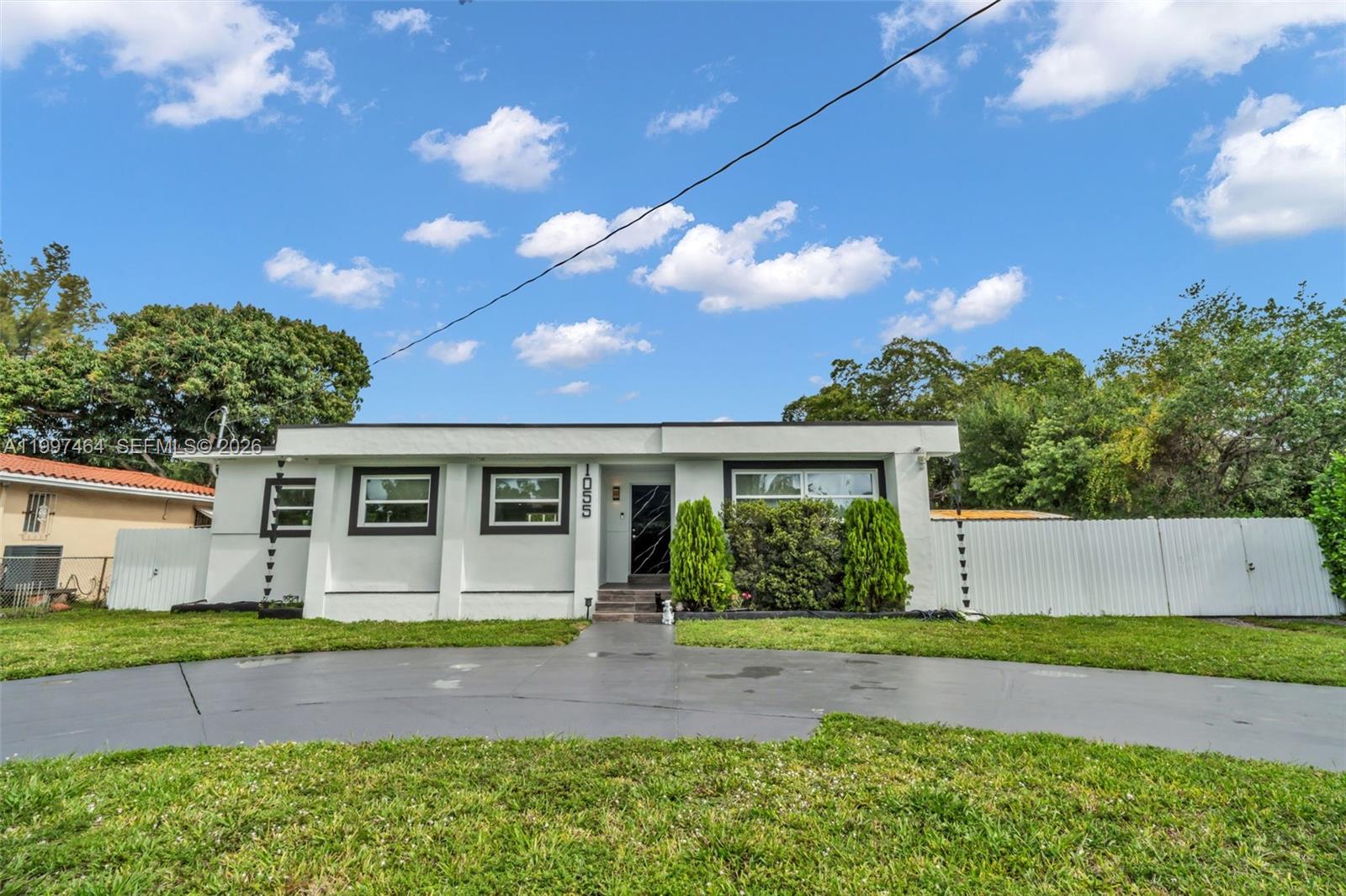 A single-story white house with a dark-trimmed front door and a curved driveway — 1055 NE 144th St, North Miami FL 33161, NORTH MIAMI, FL