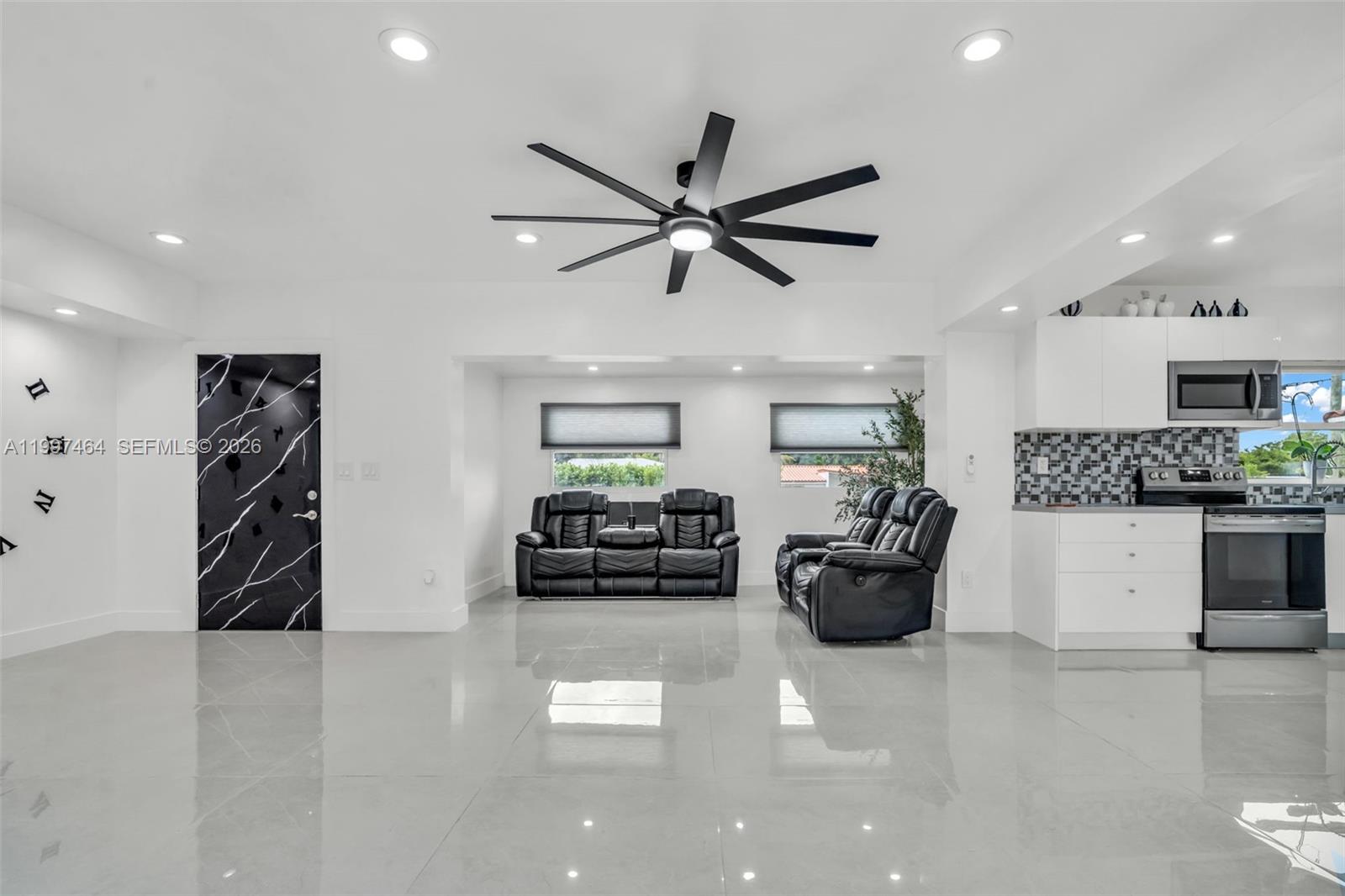 A modern open-concept living room and kitchen feature white walls, glossy tile floors, and black furniture — 1055 NE 144th St, North Miami FL 33161, NORTH MIAMI, FL
