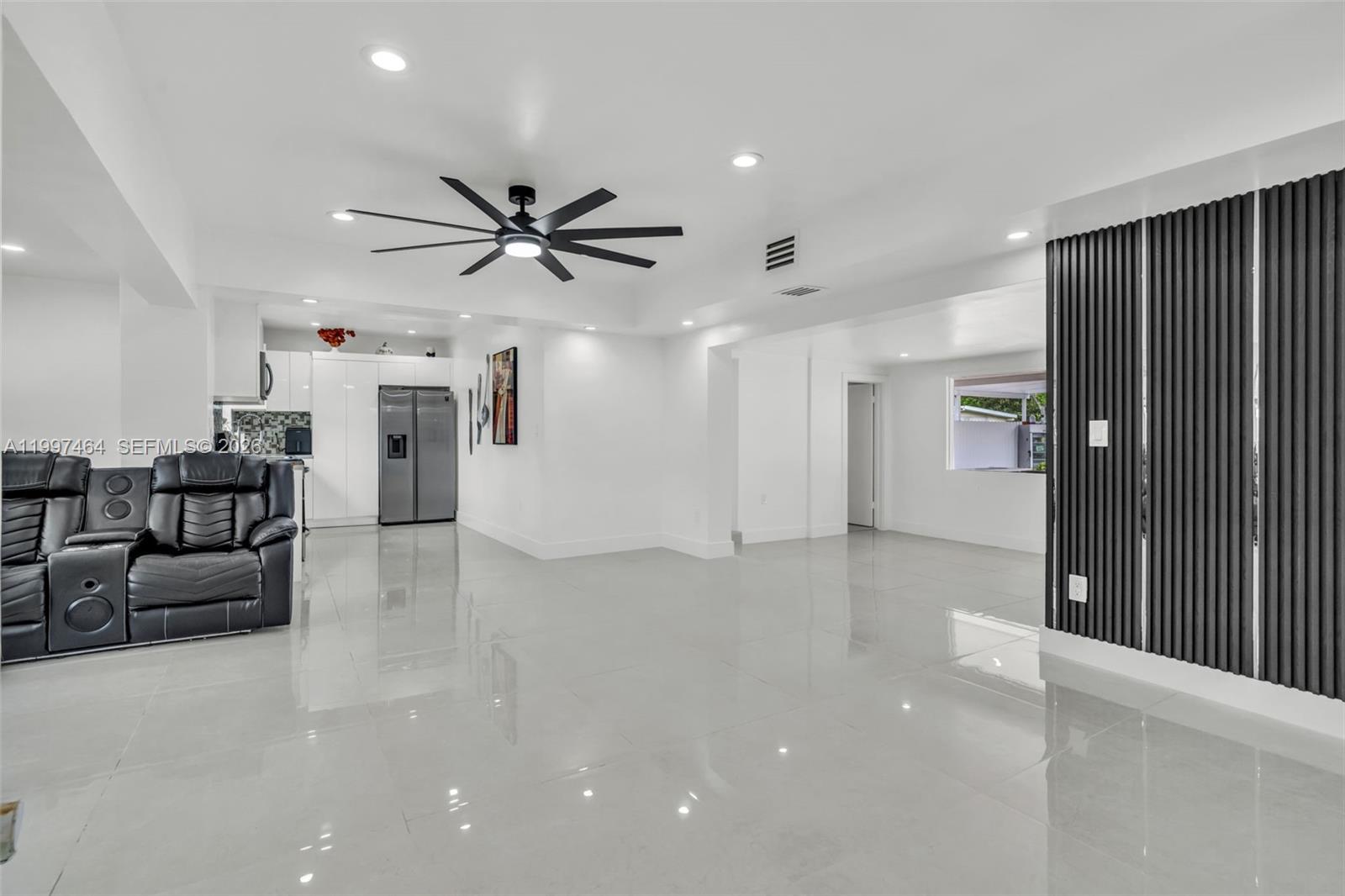 A modern living room features white tile floors, a black ceiling fan, and a slatted wall — 1055 NE 144th St, North Miami FL 33161, NORTH MIAMI, FL