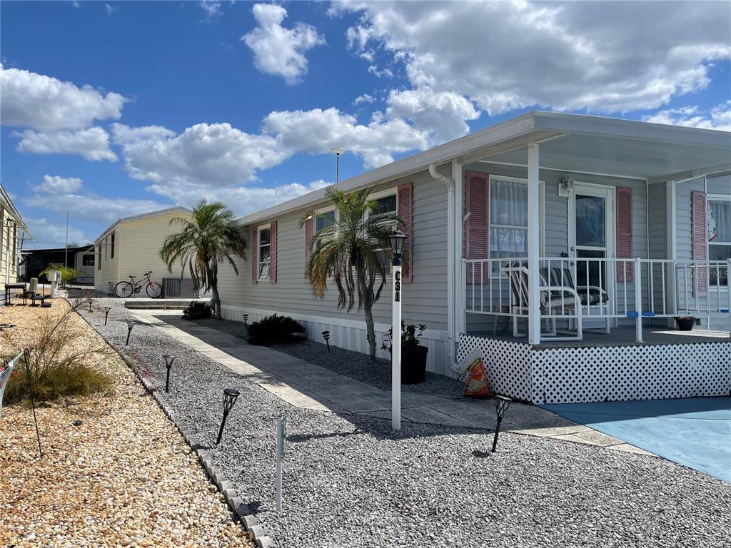 A light gray mobile home with pink shutters and a gravel yard under a blue sky — 251 PATTERSON ROAD UNIT C-31, HAINES CITY, FL