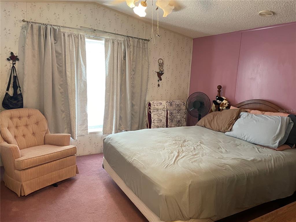A bedroom features a bed, a pink armchair, floral wallpaper, and a purple accent wall — 251 PATTERSON ROAD UNIT C-31, HAINES CITY, FL