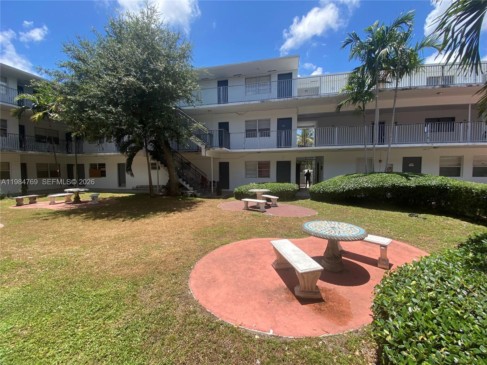 An outdoor courtyard features several stone tables and benches on a grassy lawn — 13700 NE 6th Ave # 104, North Miami FL 33161, NORTH MIAMI, FL