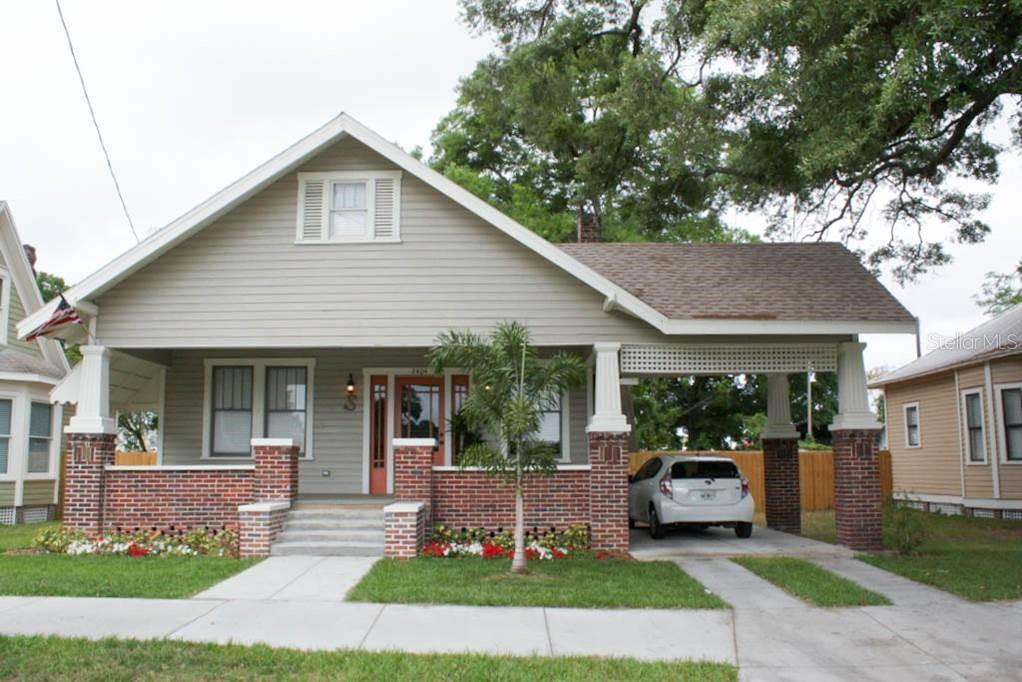 A single-story bungalow with a brick-based front porch, a carport, and gray horizontal siding — 2404 N MORGAN STREET, TAMPA, FL