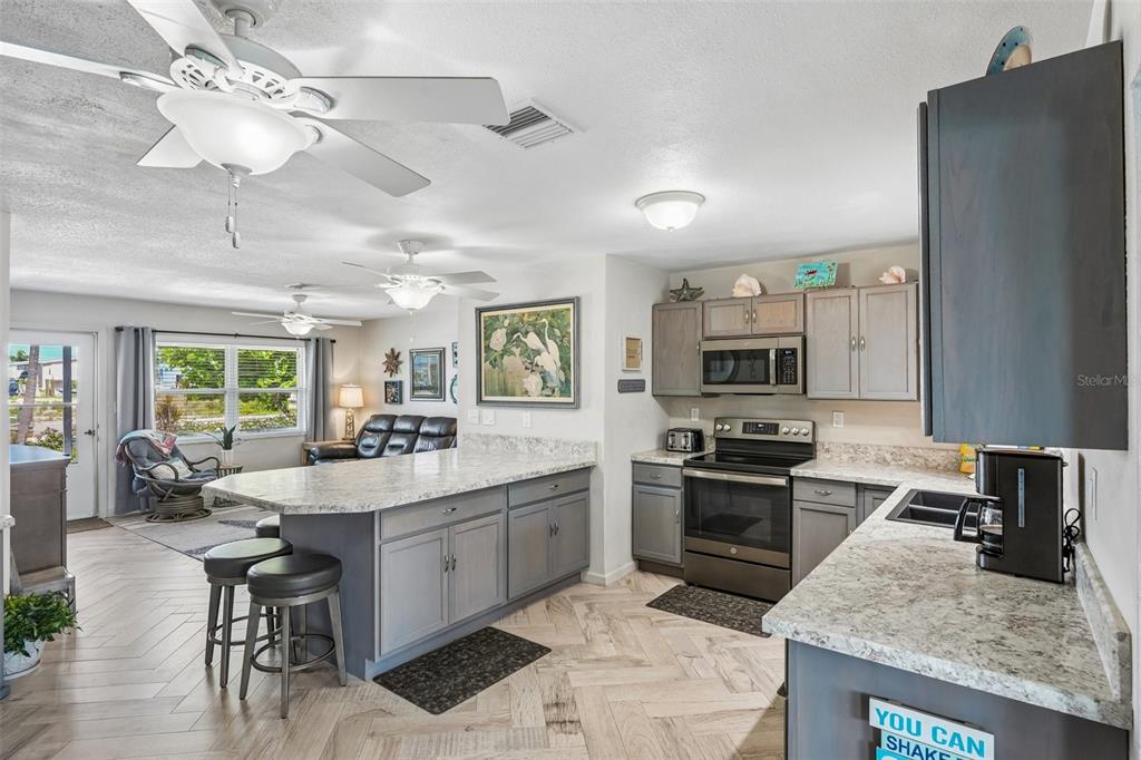 A kitchen with gray cabinets and stone countertops opens into a living area with fans — 3050 YORK ROAD, ST JAMES CITY, FL