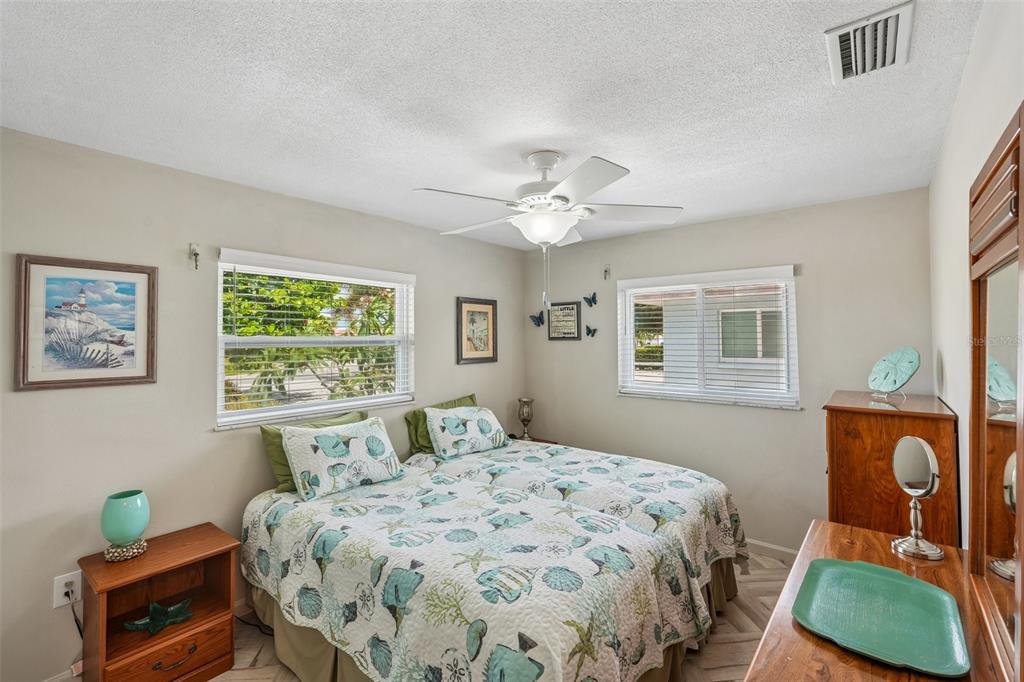 A bedroom features two twin beds with seashell-patterned quilts, wooden furniture, and two windows — 3050 YORK ROAD, ST JAMES CITY, FL