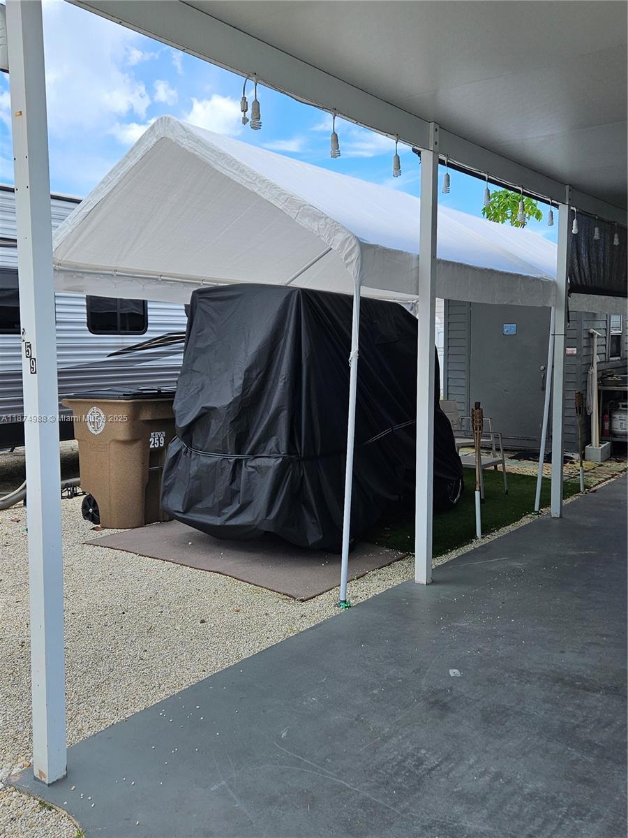 A white canopy covers a black-covered golf cart parked on a gravel and turf lot — 325 Calusa St   #259, Key Largo FL 33037, KEY LARGO, FL