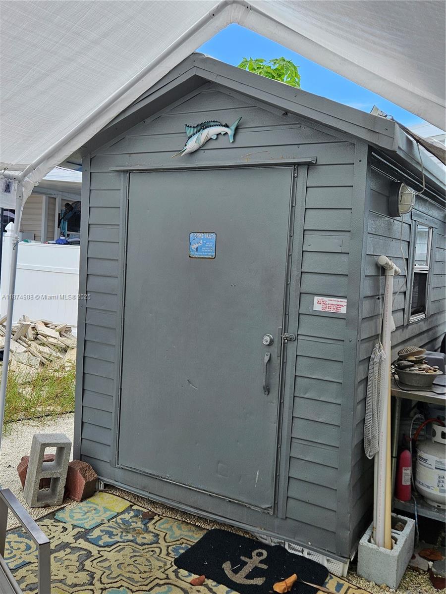 A gray wooden storage shed with a fish decoration sits under a white canopy — 325 Calusa St   #259, Key Largo FL 33037, KEY LARGO, FL