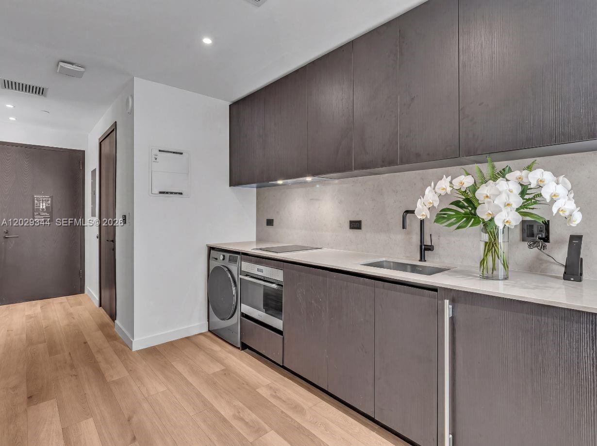 A modern kitchen features dark wood cabinetry, light stone countertops, and integrated stainless steel appliances — 20 NE 11th St # 2606A, Miami FL 33132, MIAMI, FL