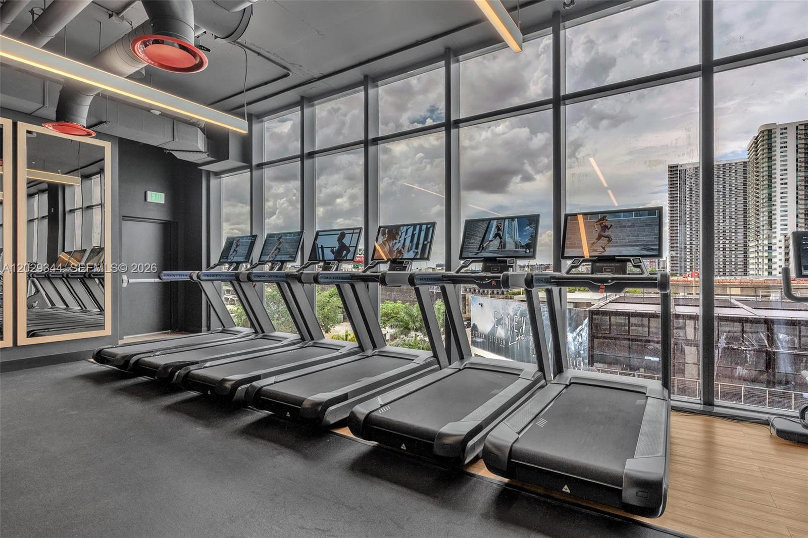 A gym room features a row of treadmills facing floor-to-ceiling windows overlooking a city skyline — 20 NE 11th St # 2606A, Miami FL 33132, MIAMI, FL