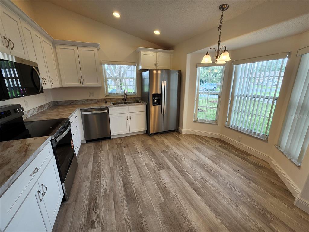 A kitchen with white cabinets, stainless steel appliances, and wood-look flooring near a dining area — 4694 PRAIRIE POINT BOULEVARD, KISSIMMEE, FL