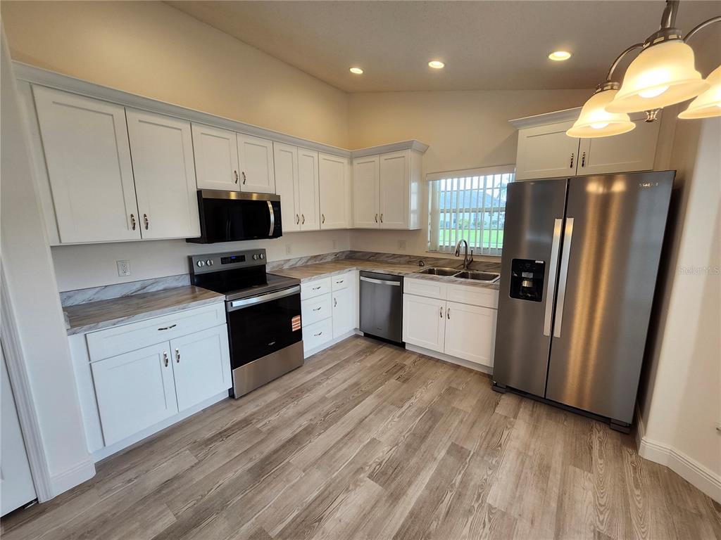 A kitchen features white cabinets, stainless steel appliances, and wood-look flooring — 4694 PRAIRIE POINT BOULEVARD, KISSIMMEE, FL