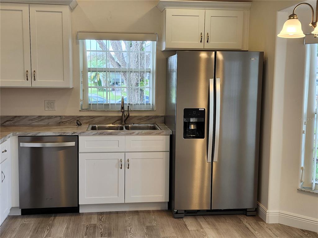A kitchen features white cabinets, stainless steel appliances, a double sink, and wood-look flooring — 4694 PRAIRIE POINT BOULEVARD, KISSIMMEE, FL