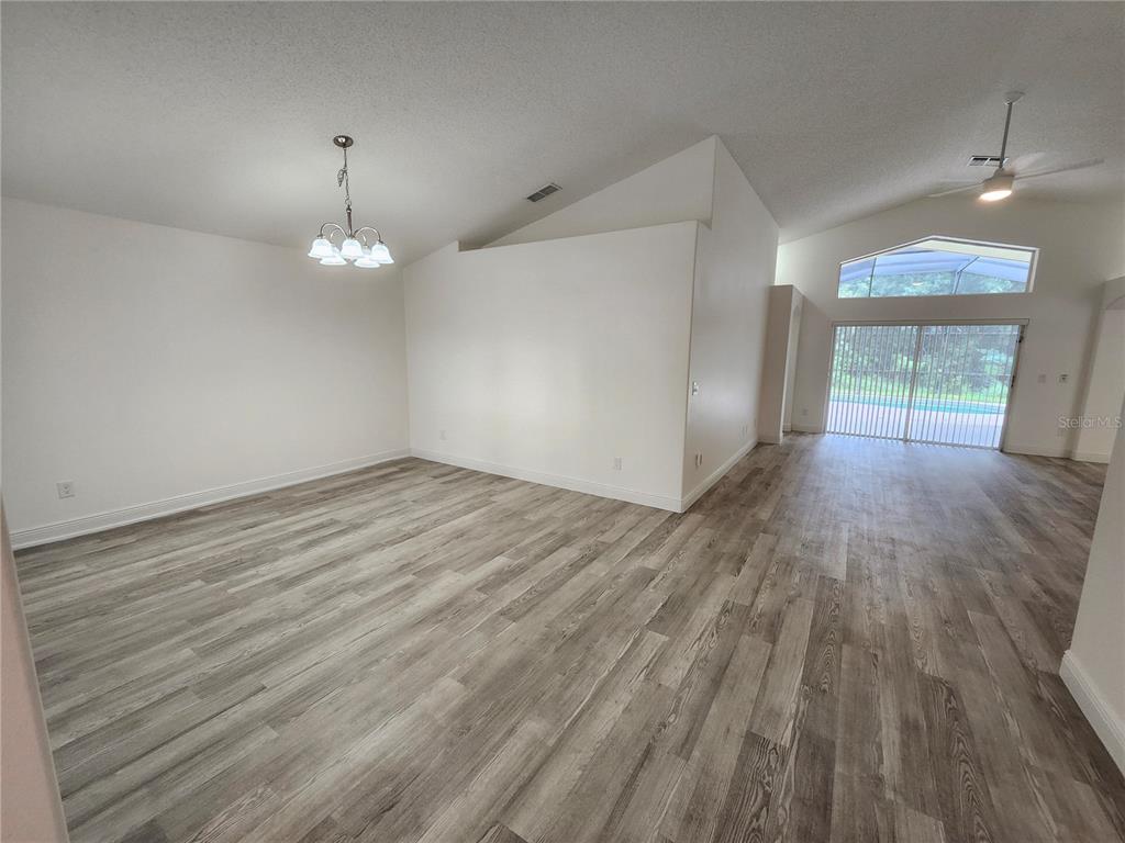 An open living area features light wood-look flooring, white walls, and a vaulted ceiling — 4694 PRAIRIE POINT BOULEVARD, KISSIMMEE, FL