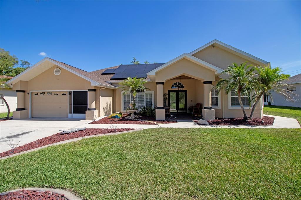 A single-story house with a tan exterior, a two-car garage, and solar panels on the roof — 8933 THOREAU PLACE, HUDSON, FL