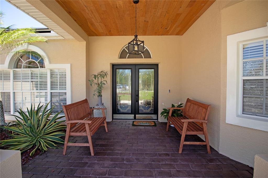 A covered front porch features a brick floor, wood ceiling, and two wooden benches — 8933 THOREAU PLACE, HUDSON, FL
