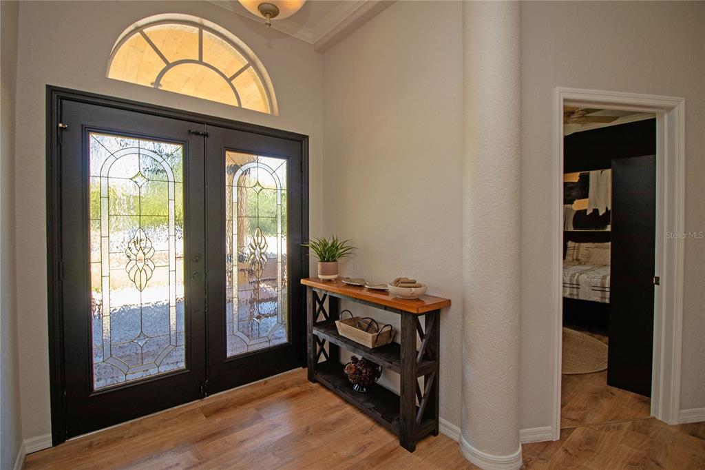 An entryway features double glass-paneled doors, a wooden console table, and a rounded support column — 8933 THOREAU PLACE, HUDSON, FL
