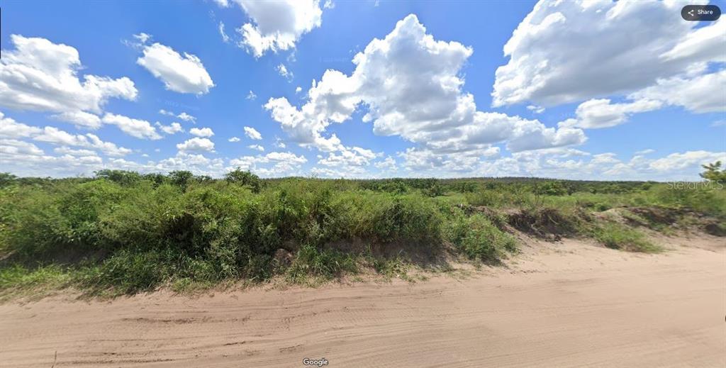 A dirt road runs alongside a vacant, overgrown lot under a bright, cloudy blue sky — HOLOPAW GROVES ROAD, ST CLOUD, FL