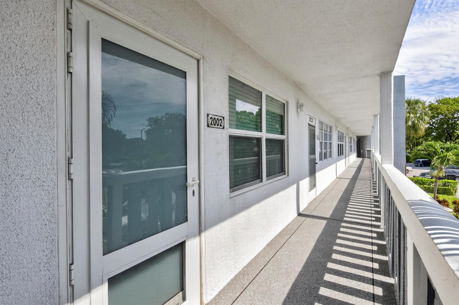 A white exterior walkway features a glass-paneled door labeled 2002 and a metal railing — 2002 Berkshire A # 2002, Deerfield Beach FL 33442, DEERFIELD BEACH, FL