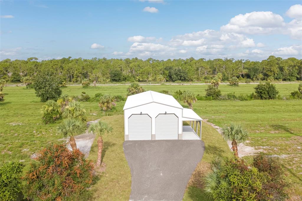An aerial view of a white metal garage with two roll-up doors and a side carport — 7023 AUSTRIAN BOULEVARD, PUNTA GORDA, FL