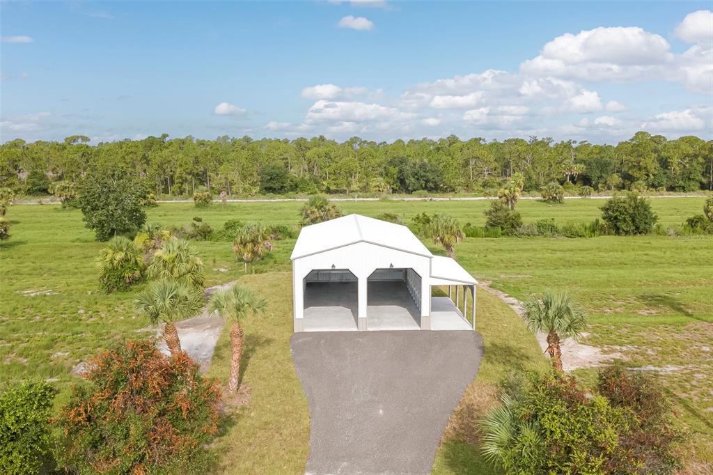 An aerial view shows a white metal garage with three bays situated on a grassy lot — 7023 AUSTRIAN BOULEVARD, PUNTA GORDA, FL