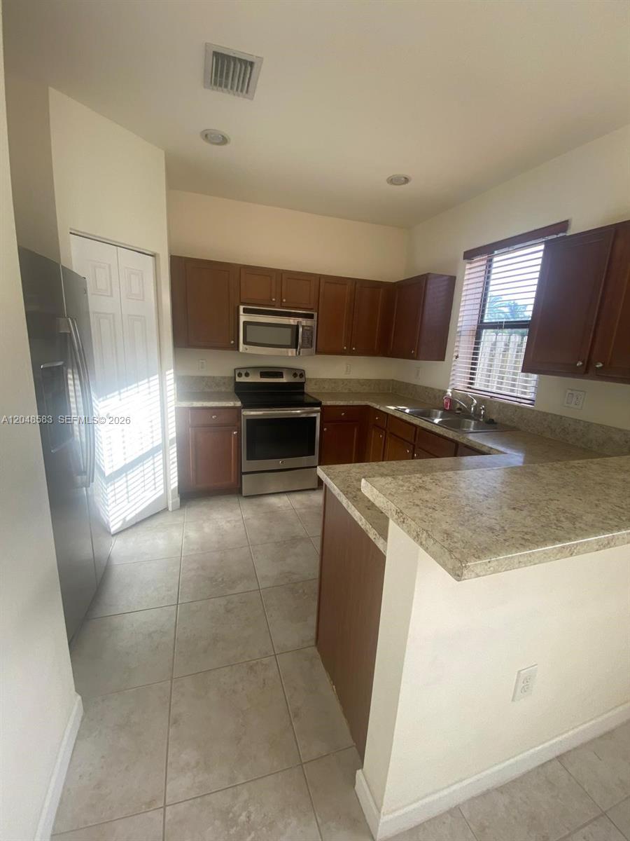 A kitchen features wood cabinets, stainless steel appliances, and a light-colored laminate countertop — MIAMI, FL