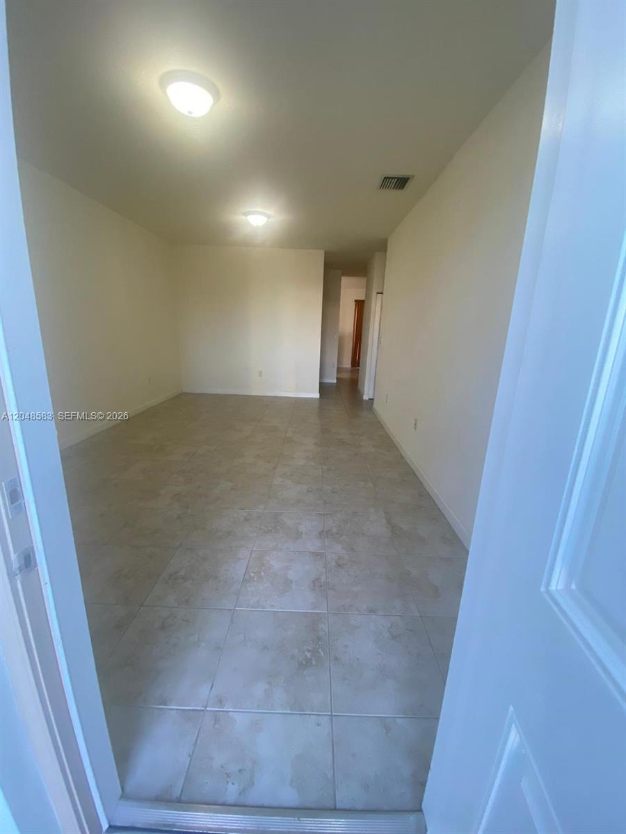 An empty room features light-colored tile flooring, white walls, and two ceiling-mounted light fixtures — MIAMI, FL