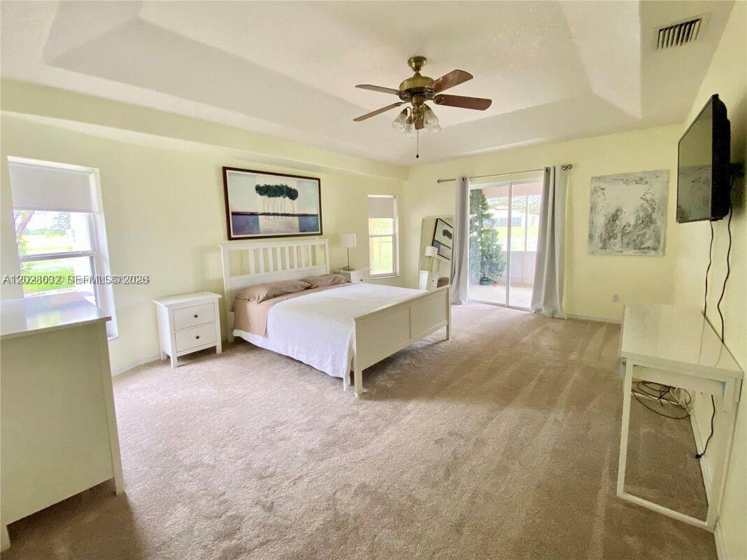 A spacious bedroom features a white bed, beige carpet, and sliding glass doors to a patio — 12245 NE 56th Ave, Okeechobee FL 34972, OKEECHOBEE, FL