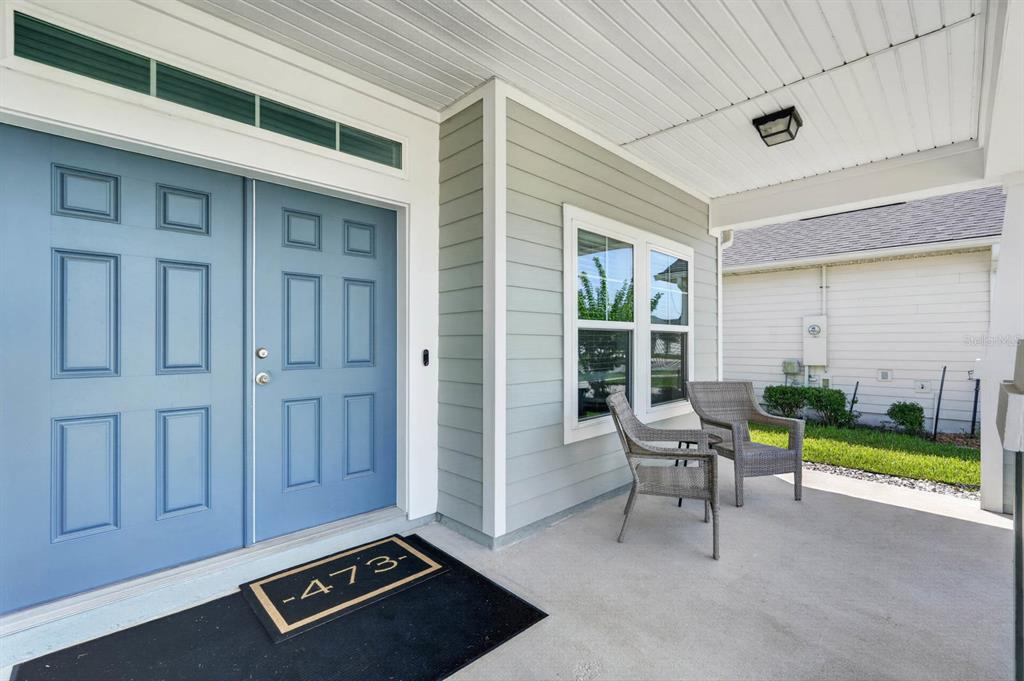 A covered front porch features a blue double door, light gray siding, and two chairs — 473 GRAND LANDINGS PARKWAY, PALM COAST, FL