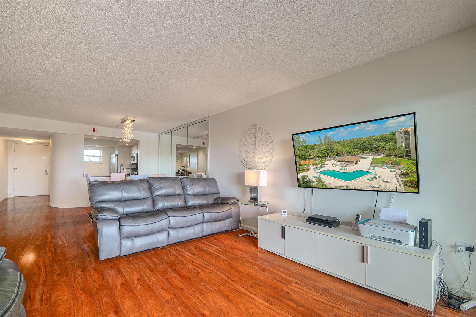 A living room features a gray leather sofa, wood flooring, and a wall-mounted television — 3930 Inverrary Boulevard # d, Lauderhill FL 33319, LAUDERHILL, FL