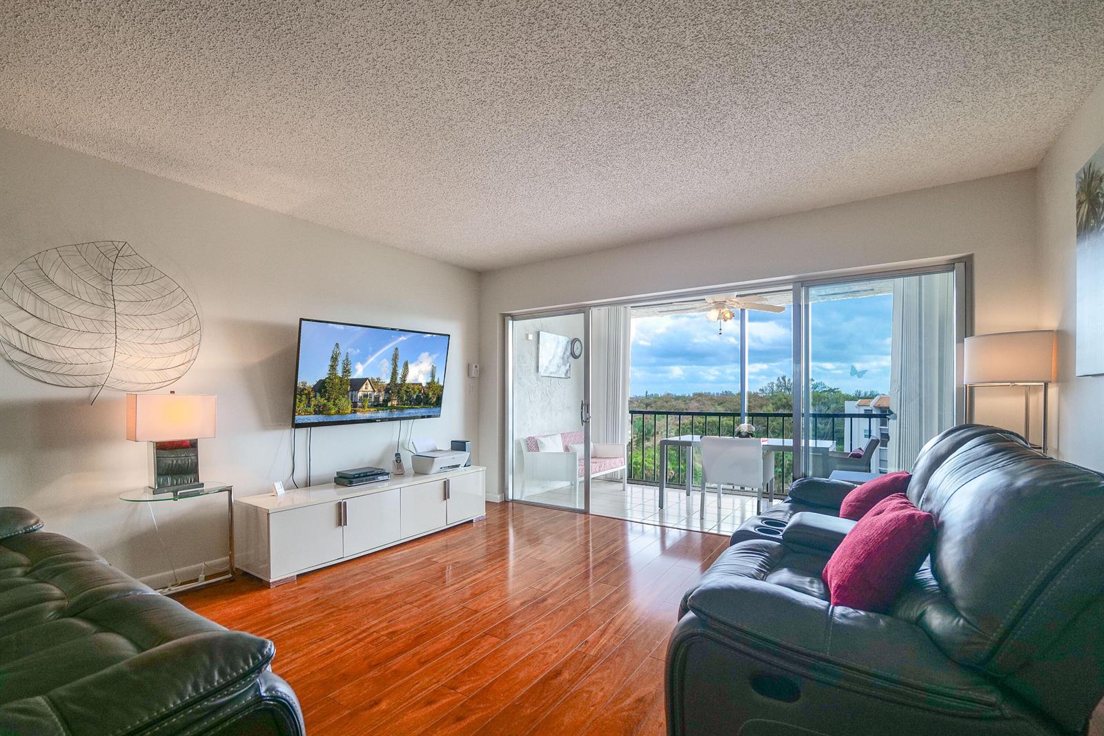 A living room with hardwood floors, a wall-mounted television, and a balcony with outdoor seating — 3930 Inverrary Boulevard # d, Lauderhill FL 33319, LAUDERHILL, FL