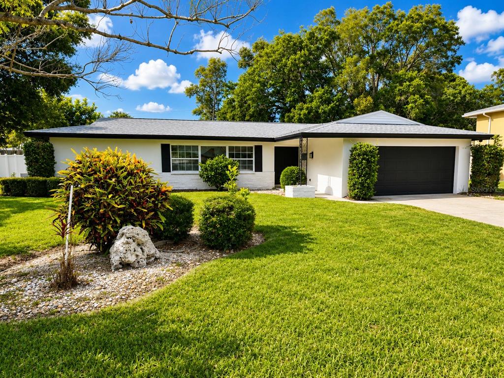 A single-story white house with a black garage door and a landscaped front yard — 810 ALLAMANDA DRIVE, LARGO, FL