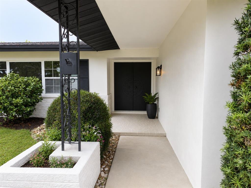 A white house exterior features a black double door, a decorative metal post, and landscaping — 810 ALLAMANDA DRIVE, LARGO, FL