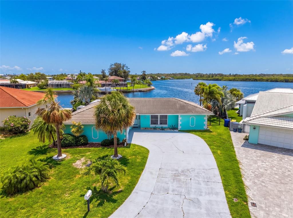 A turquoise waterfront house with a tiled roof and a concrete driveway under a sky — 4956 GALLEON COURT, NEW PORT RICHEY, FL