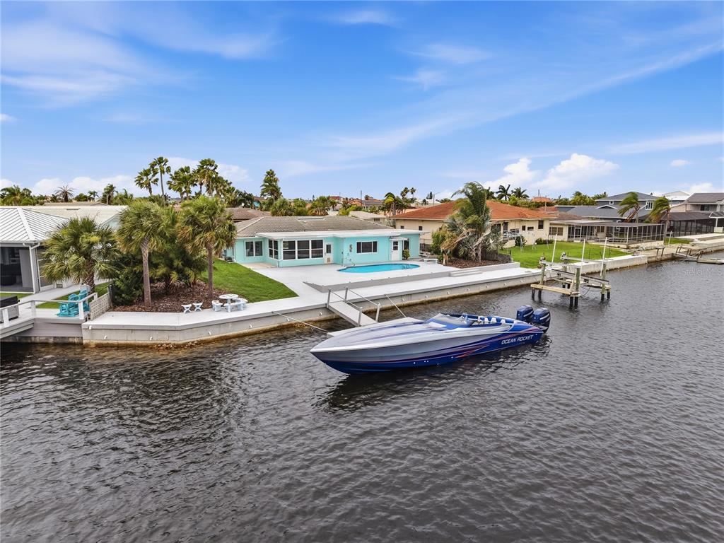 A light blue waterfront house features a swimming pool, concrete patio, and a docked boat — 4956 GALLEON COURT, NEW PORT RICHEY, FL