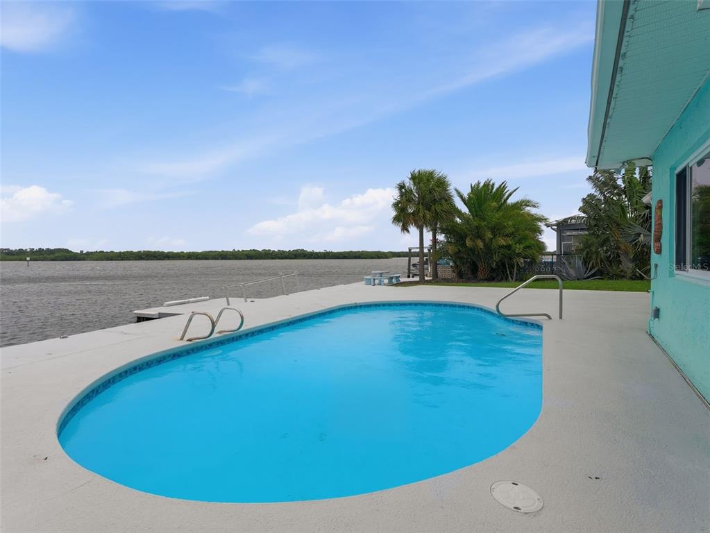 An outdoor swimming pool sits on a concrete deck overlooking a large body of water — 4956 GALLEON COURT, NEW PORT RICHEY, FL
