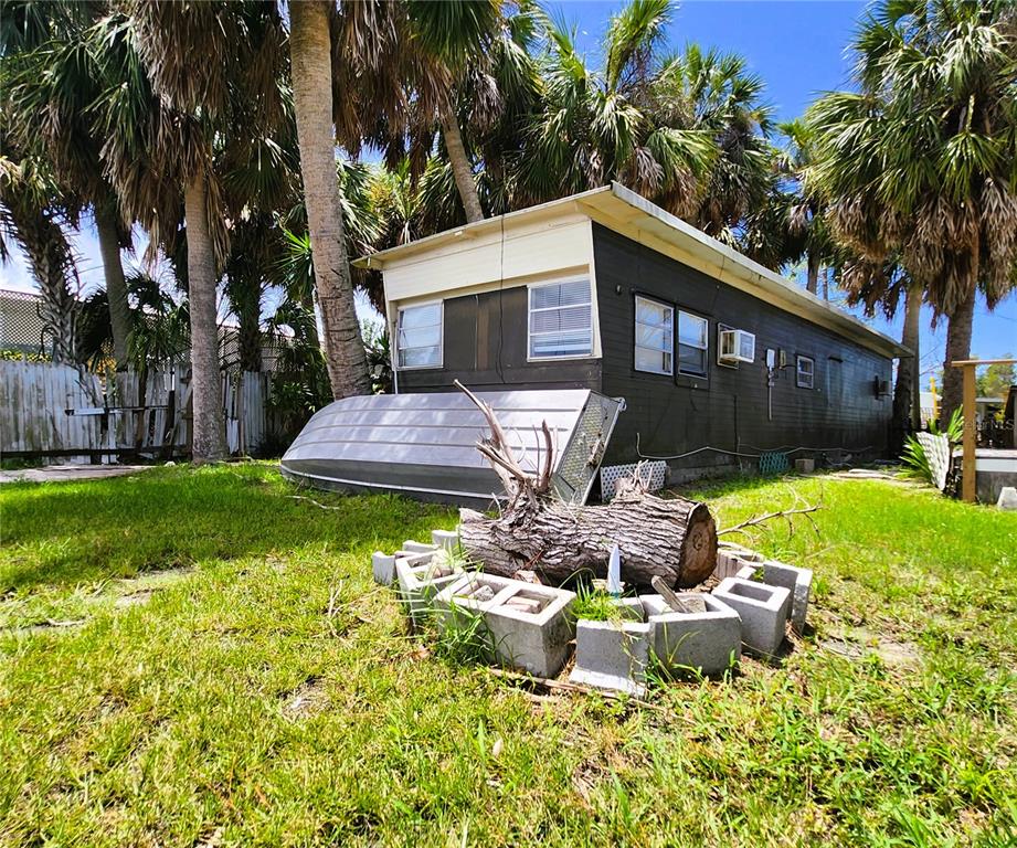 A dark-sided mobile home sits in a grassy yard with a boat and log fire pit — 6977 EDGEWATER DRIVE, NEW PORT RICHEY, FL