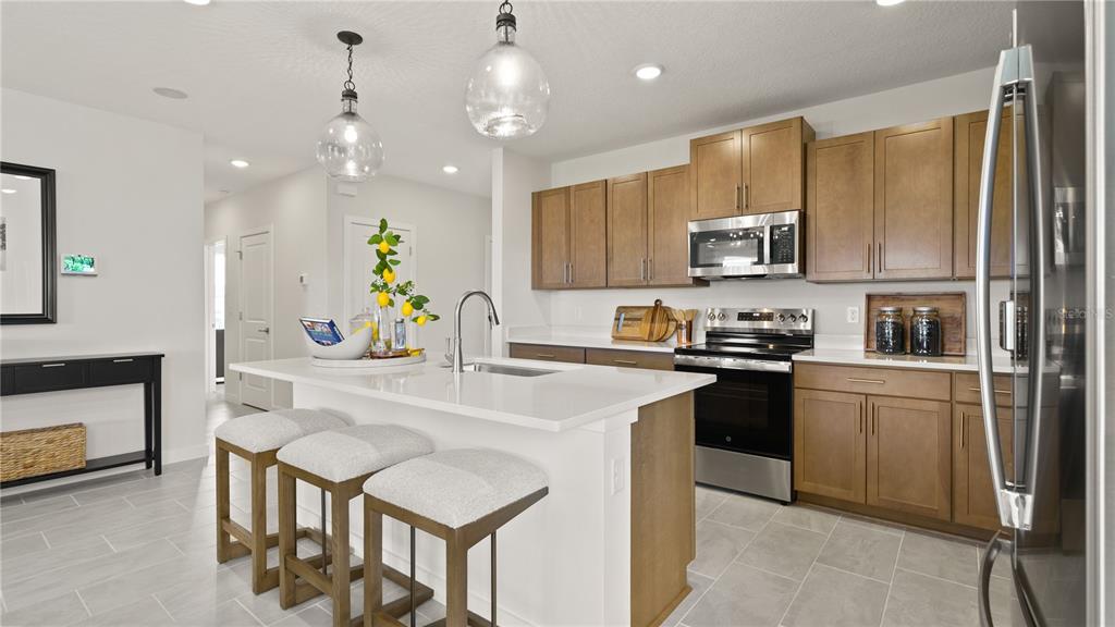 A modern kitchen features wood cabinets, a white quartz island with bar stools, and stainless appliances — 2261 CROWN ROCK BLUFF DRIVE, LAKE HAMILTON, FL