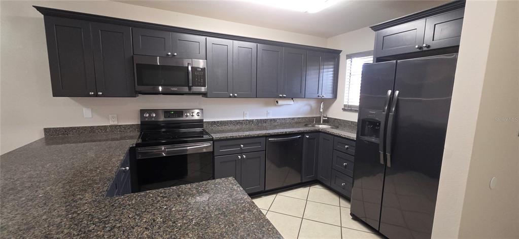 A kitchen with dark cabinets and a peninsula overlooks an open living area with tile — 6033 34TH STREET W UNIT 136, BRADENTON, FL