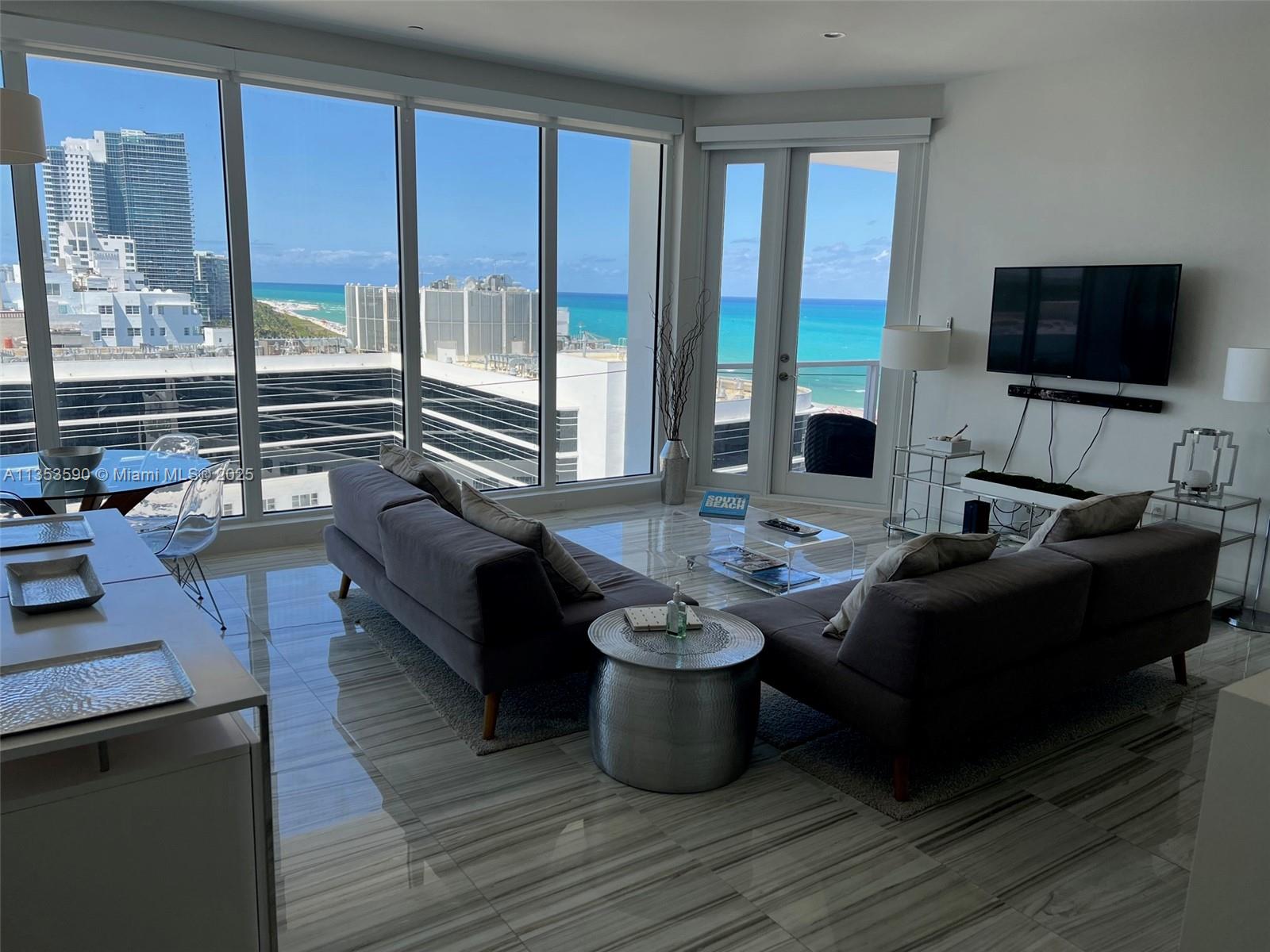 A modern living room features gray sofas, marble floors, and floor-to-ceiling windows overlooking the ocean — 100 Lincoln Rd, Miami Beach FL 33139, MIAMI BEACH, FL