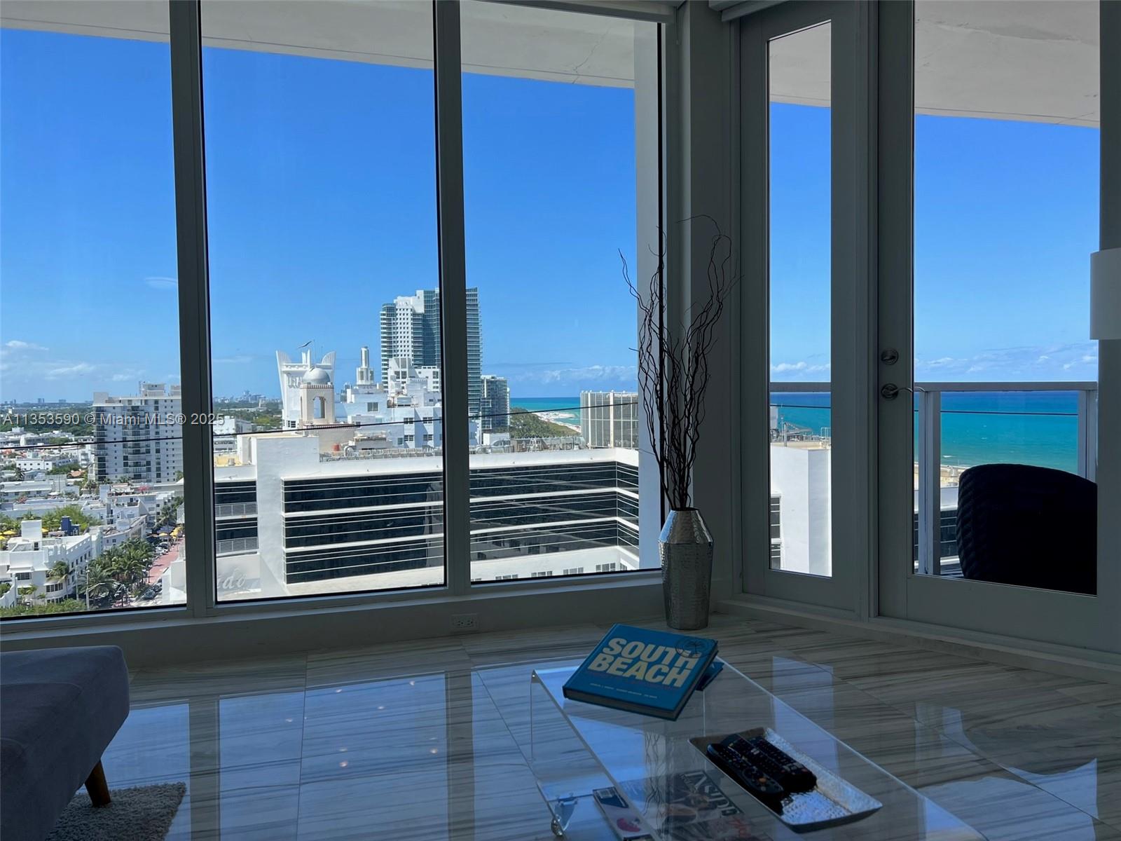 A living room with marble floors features floor-to-ceiling windows overlooking the ocean and city — 100 Lincoln Rd, Miami Beach FL 33139, MIAMI BEACH, FL