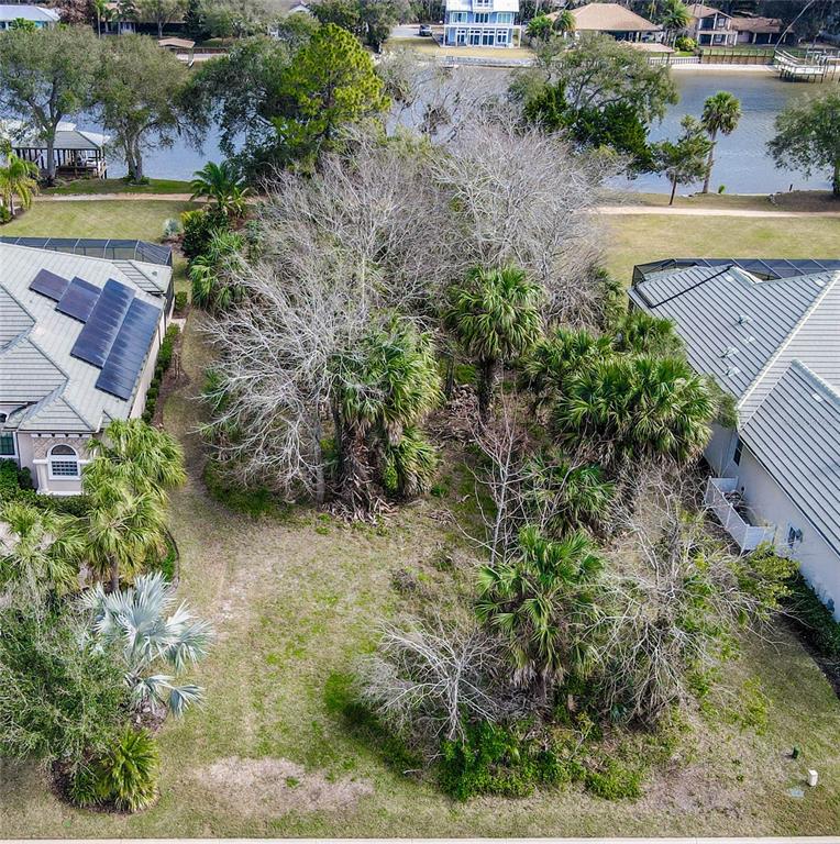 An aerial view shows a vacant, tree-filled residential lot situated between two houses near water — 121 LONGVIEW WAY N, PALM COAST, FL