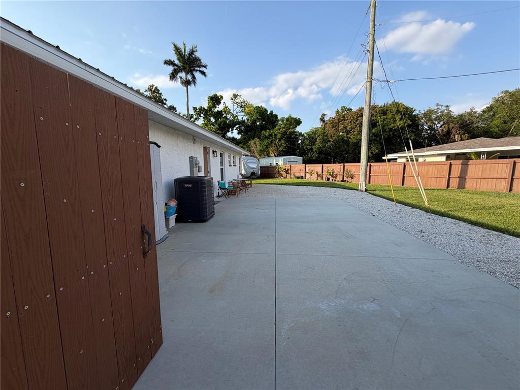 A concrete patio area sits beside a house with a wooden fence and palm tree — 4620 7TH AVENUE W, BRADENTON, FL