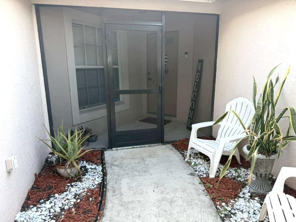 A concrete walkway leads to a screened entryway with a white chair and potted plants — 908 45TH STREET E, BRADENTON, FL