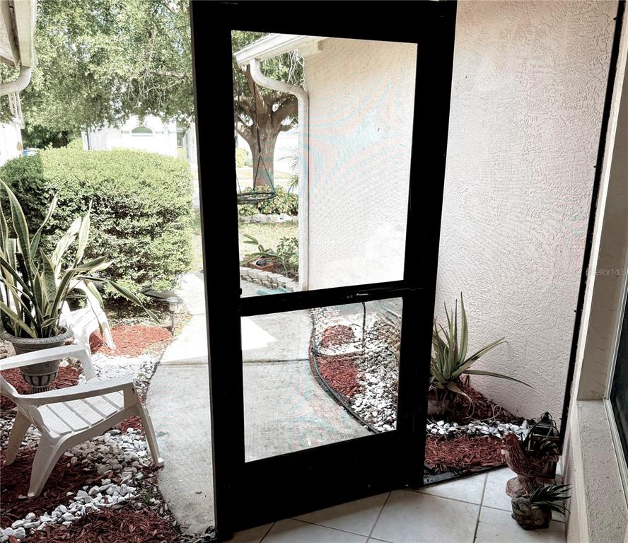 A view through a screen door shows a patio with potted plants and landscaping — 908 45TH STREET E, BRADENTON, FL