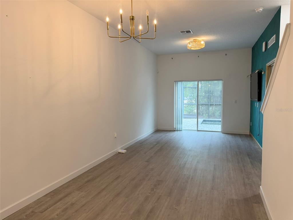 A living room features light wood-look flooring, a modern chandelier, and a sliding glass door — 368 FAMAGUSTA DRIVE, DAVENPORT, FL