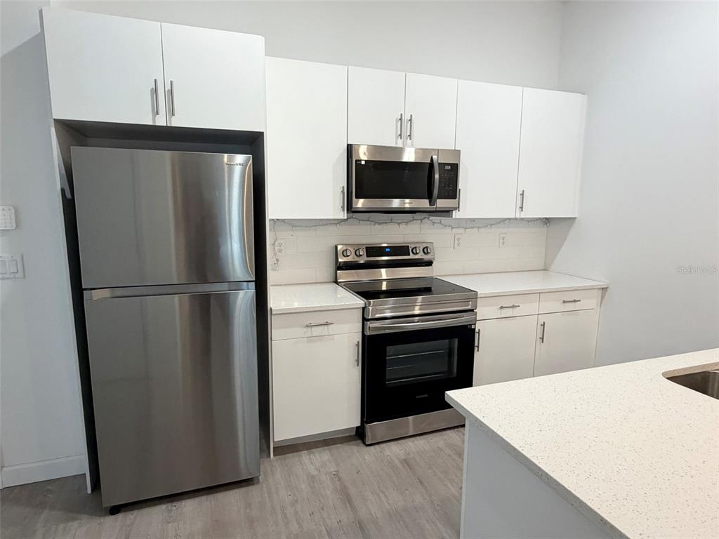 A modern kitchen features white cabinets, stainless steel appliances, and light-colored quartz countertops — 368 FAMAGUSTA DRIVE, DAVENPORT, FL