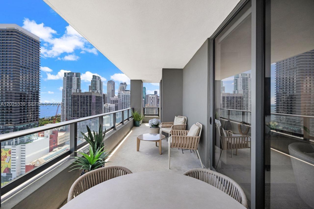 A high-rise balcony features outdoor seating, a small table, and panoramic city skyline views — MIAMI, FL