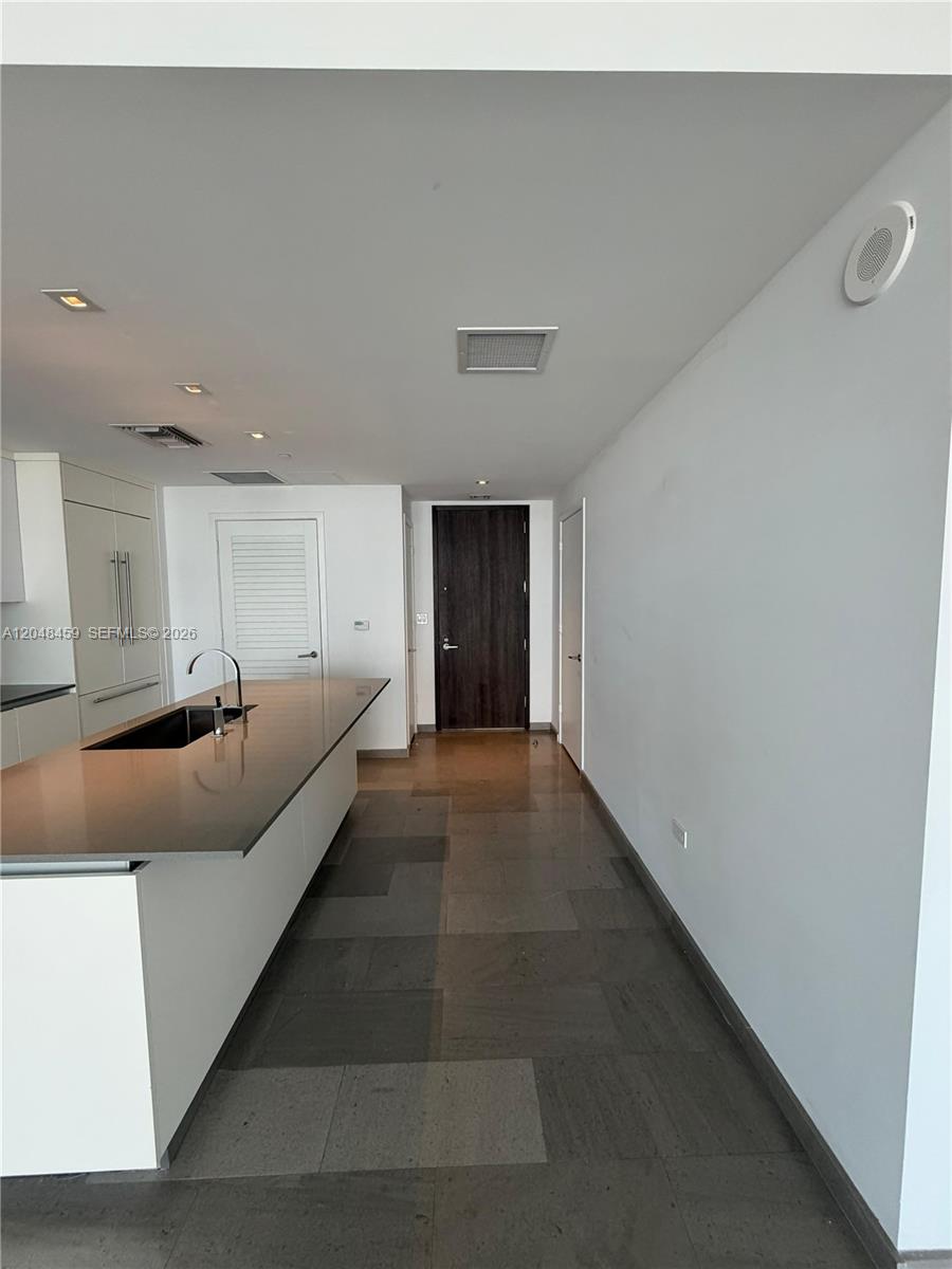 A modern kitchen features a large island with a sink and dark tile flooring — 68 SE 6th St # 2506, Miami FL 33131, MIAMI, FL