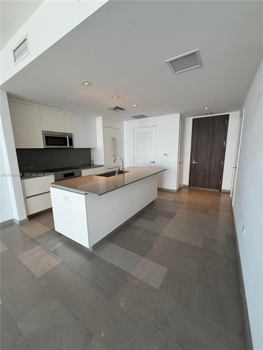 A modern kitchen features white cabinetry, a central island with a sink, and tiled flooring — 68 SE 6th St # 2506, Miami FL 33131, MIAMI, FL